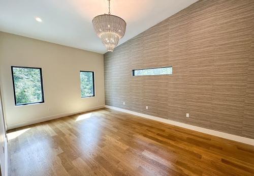 Inside of the Tulip Poplar home; WNC Parade of Homes; Modern Home; View of Primary bedroom sans furniture. Modern Chandelier hanging from ceiling; wood flooring; textured accent wall.