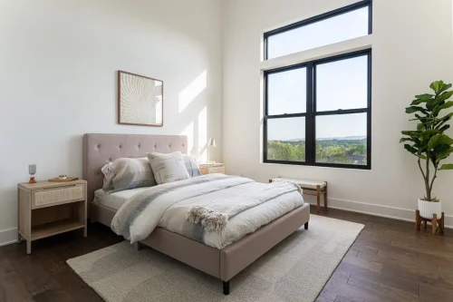 Bedroom with a tall ceiling, large black-framed window, wood flooring, and mountain views.