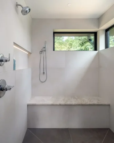 Walk-in shower with a built-in stone bench, recessed shelf, and large corner windows.