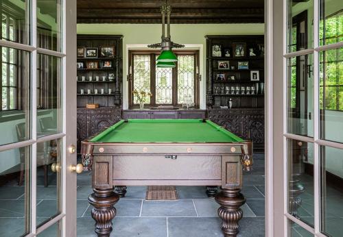 Pool table in office in Biltmore Forest. Green and french doors lead into the space. Book cases with more on the walls. Slate floor