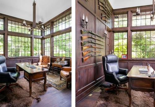 Home office with many windows, leather chair and oak table. Classic Rifles hanging on the wall behind the desk and dark wood on the walls.