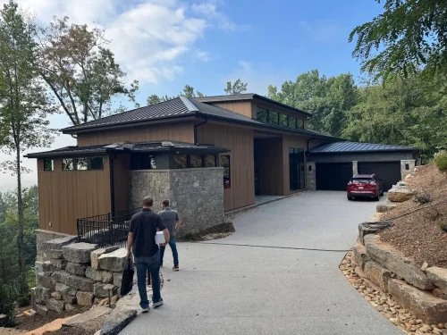 Contemporary mountain home with wood siding, stone accents, a dark metal roof, attached garage, and sloped driveway.