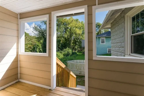 A newly finished back porch with tan siding, white trim, and wooden stairs leading to a green backyard.