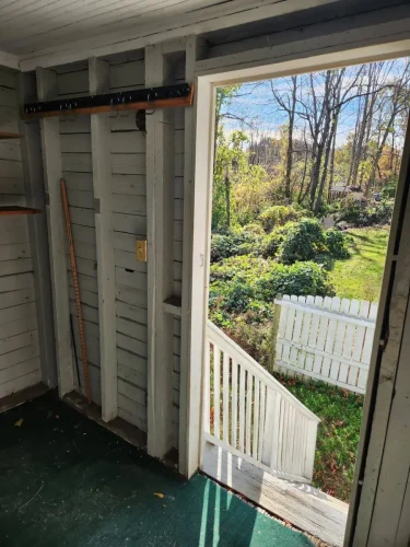 An unfinished porch with exposed framing and a view of the yard through an open doorway.