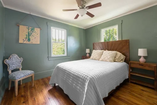 A cozy bedroom with green walls, wood floors, and a bed with a geometric headboard.