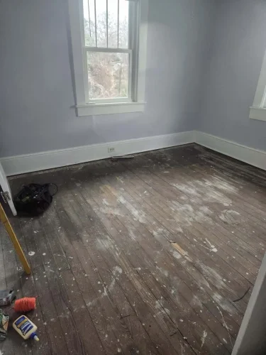 An empty bedroom with scuffed wood floors and light-colored walls.