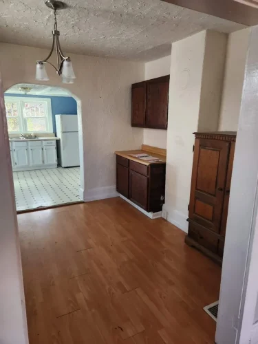 A small dining area with light wood flooring and outdated cabinetry.