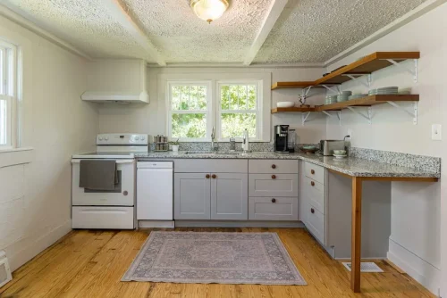 A bright kitchen with gray cabinets, open shelves, and a granite countertop.