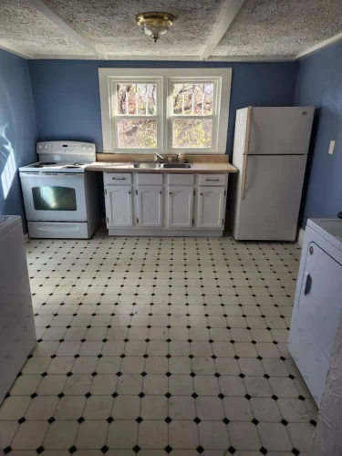A dated kitchen with blue walls, white cabinets, and checkered flooring.