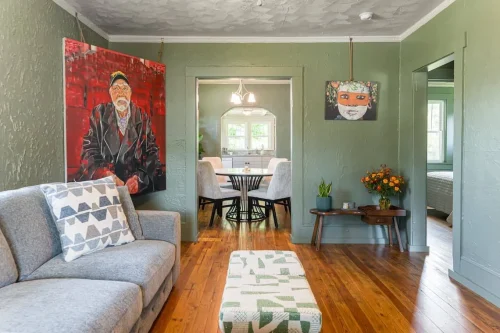 A green living room with modern art, wood floors, and a gray couch.