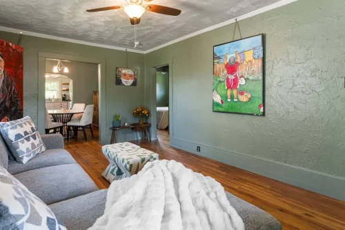 Another view of the living room with colorful artwork and a patterned ottoman.