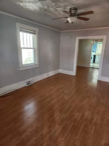 A bare room with light brown laminate flooring and gray walls.
