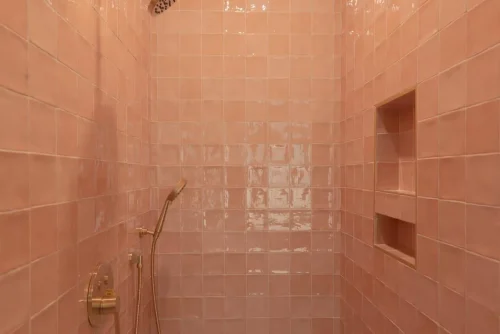 Shower with pink tile and brass fixtures.