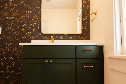 Bathroom vanity with green cabinets and floral wallpaper.