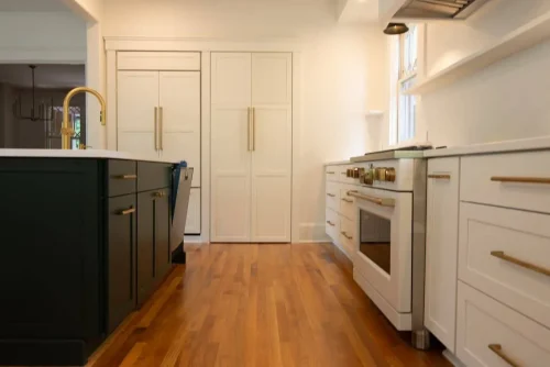 Kitchen with white cabinets, wood floors, and brass accents.