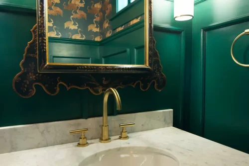 Powder room with dark green walls, marble sink, and ornate mirror.