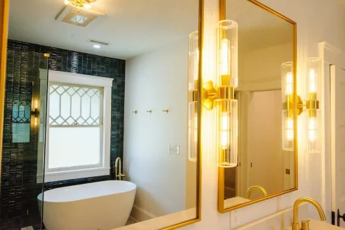 Bathroom with freestanding tub, black tile, and gold lighting.