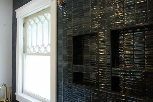 Close-up of glossy black tile wall with built-in shelving.