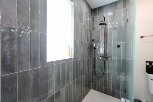 Shower with tall green tiles and bronze fixtures.