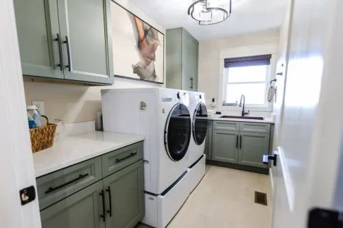 Laundry room with green cabinets and front-load washer and dryer.