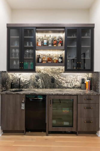 Wet bar with brown and black cabinets with sink and small fridge.