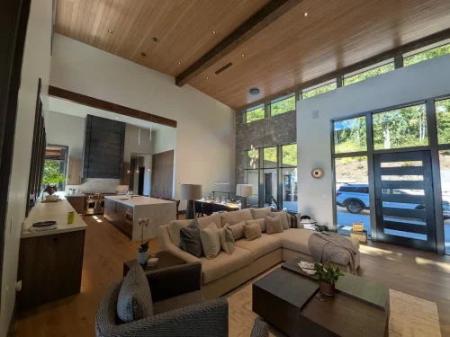 Open-concept living area with a vaulted wood ceiling, stone accent wall, large windows, and kitchen with a central island.