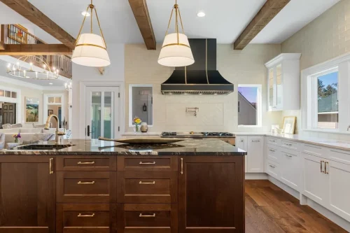 Spacious kitchen with a dark wood island, black stone countertops, white cabinetry, exposed wood ceiling beams, and gold pendant lighting.