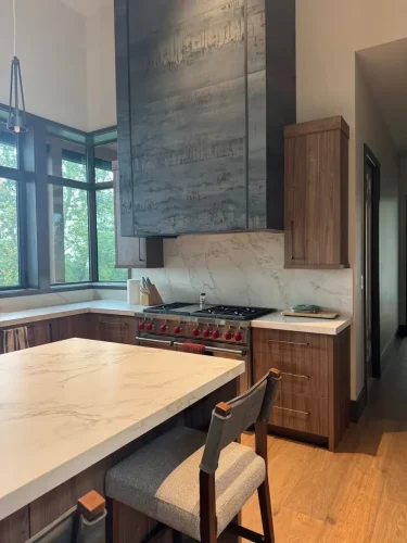 Modern kitchen with wood cabinetry, stone countertops, a large island, gas range, and oversized dark range hood.