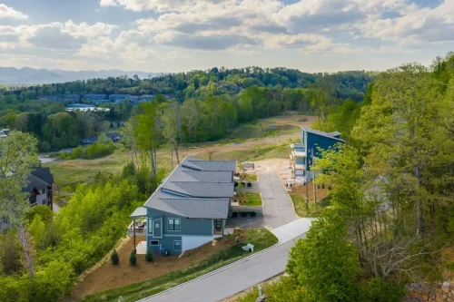 Aerial view of a hillside residential community surrounded by trees with mountain views in the distance.