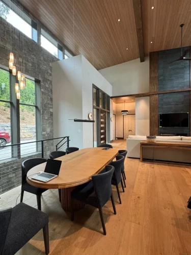 Dining space with a large wood table, vaulted wood ceiling, stone accent wall, and views into the living area.