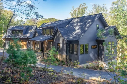 Contemporary mountain home with dark gray siding, multiple gabled rooflines, stone accents, and a covered entry surrounded by woods.