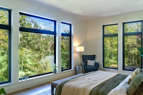 Bedroom with large black-framed windows overlooking the surrounding trees.