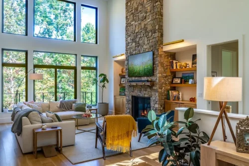 Living room with two-story windows, built-in shelving, and a floor-to-ceiling stone fireplace.