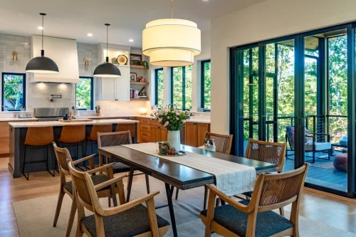 Open kitchen and dining area with wood cabinetry, a large island, black pendant lights, and doors opening to a screened porch.