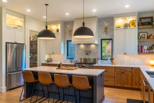 Kitchen with wood and white cabinetry, a large island with seating, white countertops, and oversized black pendant lights.