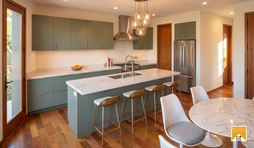 Kitchen with muted green cabinetry, white countertops, an island sink, four bar stools, and glass pendant lights.