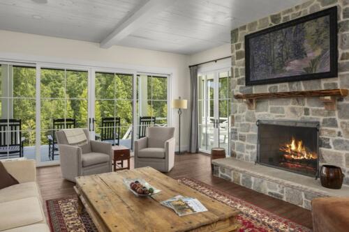 Room with a lot of windows, a stone fireplace and furniture.