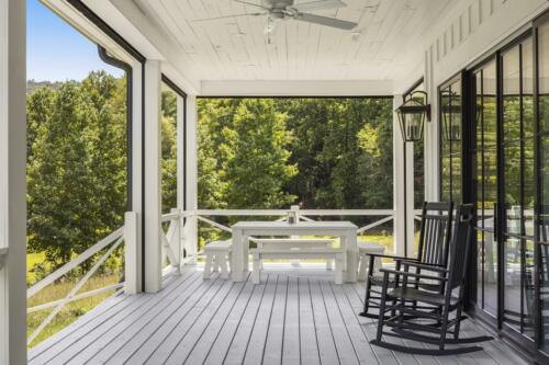 Porch with white table and black rockers overlooking trees.