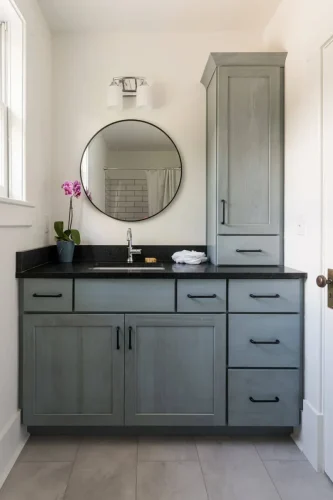 Modern bathroom with gray vanity, round mirror, and black countertop.