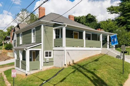 Restored green house with white trim and yellow door on a hillside.