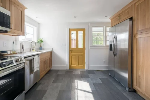 Bright kitchen with wood cabinets, stainless appliances, and yellow door.