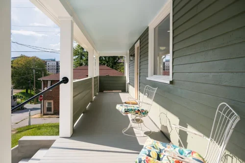 Covered porch with green siding, white trim, and colorful chairs.