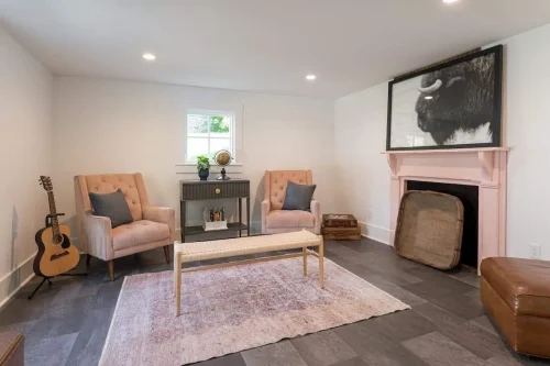 Modern study with pink fireplace, soft chairs, and framed bison artwork.