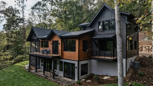 Modern mountain home with black siding and natural wood accents, tucked into a wooded hillside with multiple decks and large windows.