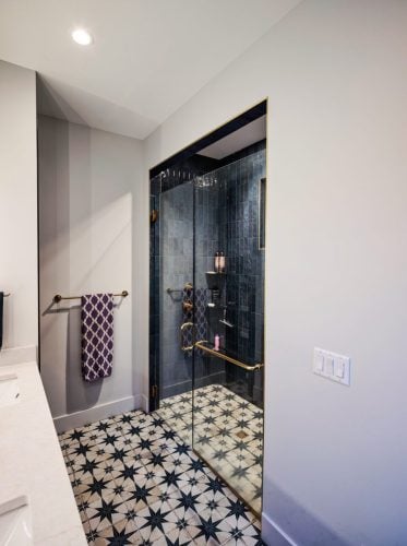 Stylish bathroom with patterned tile floor, glass shower with deep blue tile, and brass fixtures.