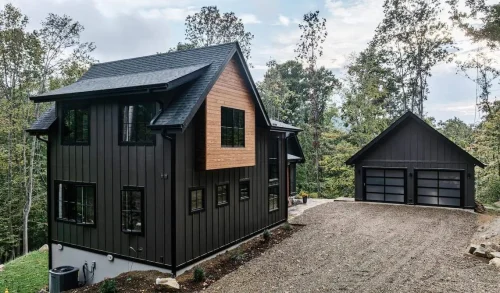 Contemporary mountain retreat with dark vertical siding, natural wood paneling, and detached garage at the top of a gravel drive.