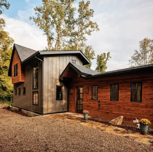 Front entry with mix of wood and metal siding, modern glass door, and stone walkway framed by planters.