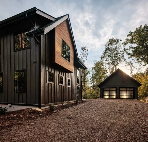 Detached two-car garage with modern dark siding and frosted glass doors, blending into wooded surroundings.