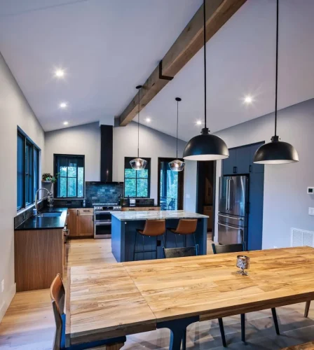 Open kitchen with dark cabinets, marble island, pendant lighting, and large windows overlooking the forest.