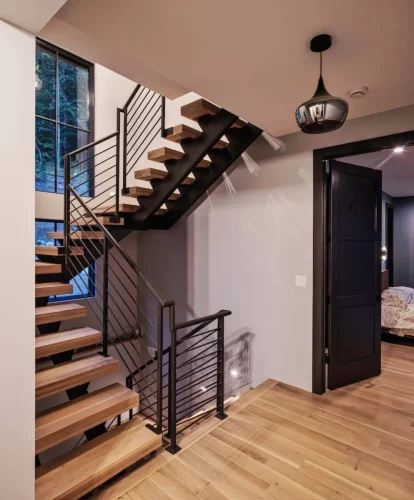 Floating wood staircase with sleek black metal railing and modern lighting detail.